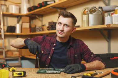 Multimetre elektrikçi için. Beyaz genç adam ekose gömlek, siyah T-shirt dijital elektronik mühendisi farklı araçları ile ahşap masa atölyesinde tamir, lehimleme bilgisayar Pc anakart.