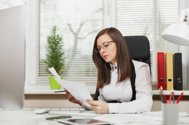 Takım elbise ve tablet ile masaya oturan gözlük güzel ciddi ve dalmış Kahverengi saç iş kadını ışık Office belgeleri ile modern monitör bilgisayarda çalışan bir kenara arıyorsunuz