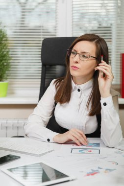 Takım elbise ve tablet ile masaya oturan gözlük güzel ciddi ve dalmış Kahverengi saç iş kadını ışık Office belgeleri ile modern monitör bilgisayarda çalışan bir kenara arıyorsunuz