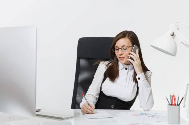 Takım elbise ve masa başında oturan gözlük güzel ciddi iş kadını ışık Office belgeleri ile çağdaş bilgisayarda çalışan cep telefonu beyaz arka plan üzerinde sorunlarını çözme konuşurken