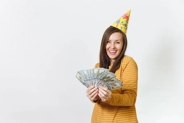 Beautiful caucasian lucky young happy woman in yellow clothes, birthday party hat holding wad of cash money, celebrating holiday on white background isolated for advertisement. Winner with dollars. — Stock Photo, Image