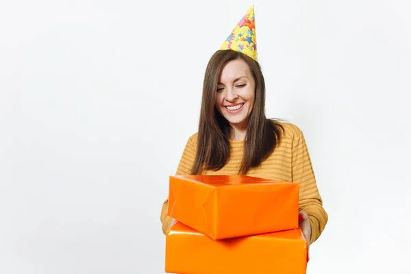 Bonita mulher feliz branca divertida jovem em roupas amarelas, chapéu de festa de aniversário segurando caixas de presente laranja com presente, celebrando e desfrutando de férias em fundo branco isolado para propaganda . — Fotografia de Stock