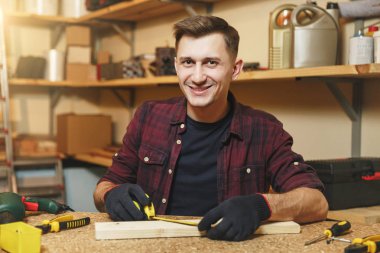 Yakışıklı beyaz delikanlı ekose gömlek, siyah T-shirt, şerit metre, ahşap masa doğrama atölyesinde çalışan ile ahşap parça uzunluğu ölçme eldiven farklı çalışma araçları ile yerleştirin..