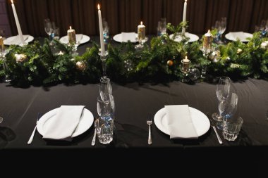 Gözlük, çatal, bıçak, peçete, mumlar ve koyu siyah masa örtüsü rahat restoranda akşam yemeği için tablo üzerinde dekoratif çiçek kapatın. Boş servis restoran tablo tabak ve bardak şarap ile