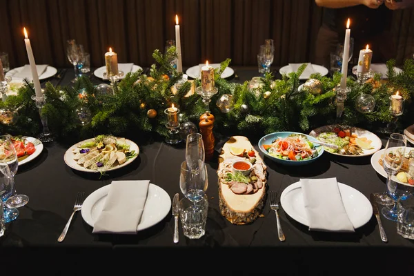 Lunettes, fourchettes, couteaux, serviettes, bougies et fleurs décoratives sur une nappe noire foncée sur la table servie pour le dîner dans un restaurant confortable. Table de restaurant avec assiettes et verre à vin . — Photo