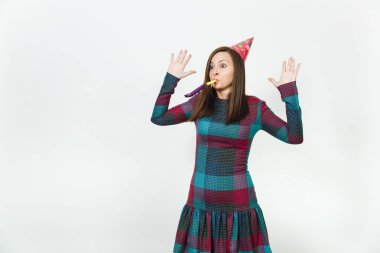 Güzel beyaz eğlence genç mutlu kadın ekose elbise ve doğum günü parti şapkası ile utangaç çekici gülümseme ve boru, kutlama ve reklam için izole beyaz arka plan üzerinde tatil keyfini.