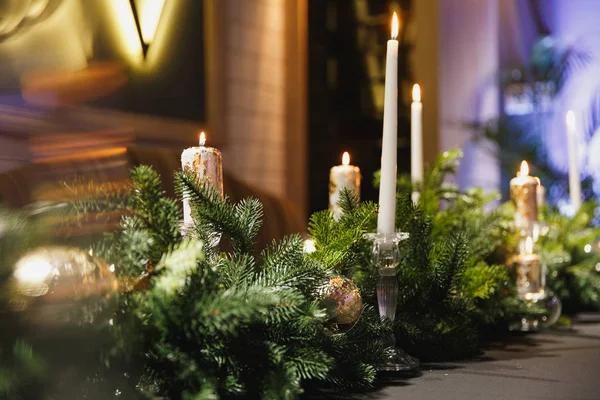 Weihnachtlich dekorierter Tisch mit grünen Fichtenzweigen, Kugeln und brennender Kerze im gemütlichen Restaurant. — Stockfoto