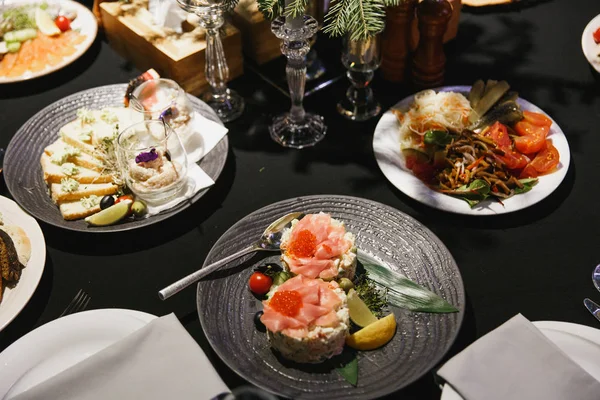 Restaurant food on gray and white plates closeup on dark black tablecloth on table served for dinner in cozy luxury restaurant. Perfect vegetables, cheese, snacks, caviar. Eating out concept.