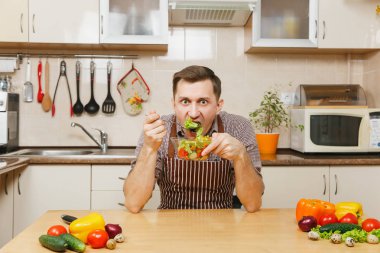 Işık mutfakta yemek çekici aç Beyaz delikanlı kase sebze salatası ile masada oturan önlük, kahverengi gömlekli. Diyet kavramı. Sağlıklı bir yaşam tarzı. Evde yemek. Yemek hazırlamak.