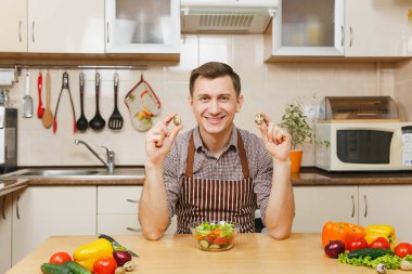 Bıldırcın yumurta, hafif mutfakta holding beyaz yakışıklı genç sebze salatası ile masada oturan bir önlük, kahverengi gömlekli. Diyet kavramı. Sağlıklı bir yaşam tarzı. Evde yemek. Yemek hazırlamak.
