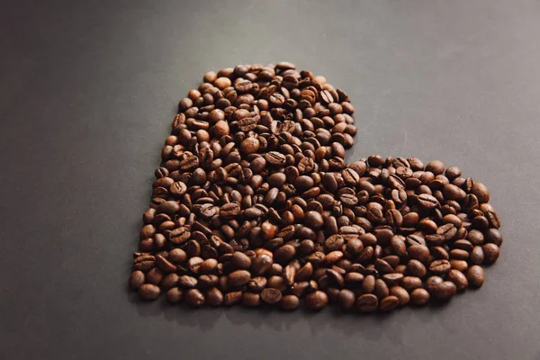 Grãos de café marrom em forma de coração isolado na textura preta ba — Fotografia de Stock