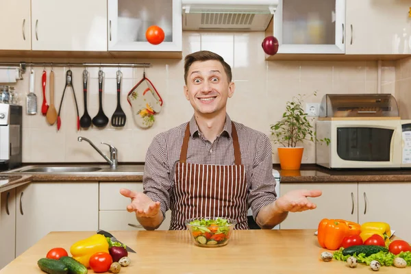 Soğan ve domates, yetişmek sebze salatası kadar ışık mutfak bıçak atma eğlenceli deli beyaz delikanlı masadan, önlük, kahverengi gömlekli. Diyet kavramı. Evde yemek. Yemek hazırlamak.