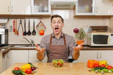 Soğan ve domates, yetişmek sebze salatası kadar ışık mutfak bıçak atma eğlenceli deli beyaz delikanlı masadan, önlük, kahverengi gömlekli. Diyet kavramı. Evde yemek. Yemek hazırlamak.