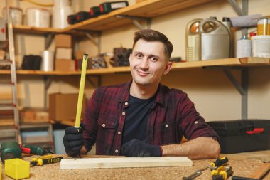 Yakışıklı beyaz delikanlı ekose gömlek, siyah T-shirt, şerit metre, ahşap masa doğrama atölyesinde çalışan ile ahşap parça uzunluğu ölçme eldiven farklı çalışma araçları ile yerleştirin..