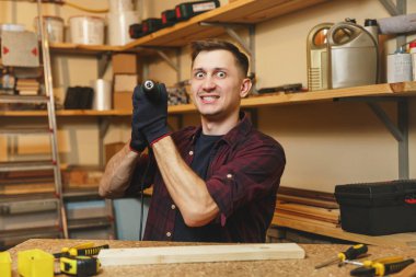 Çılgın agresif kızgın beyaz genç adam ekose gömlek, siyah T-shirt, matkap parça ahşap, ahşap masa doğrama atölyesinde çalışan ile sondaj eldiven farklı araçlarla yerleştirin..