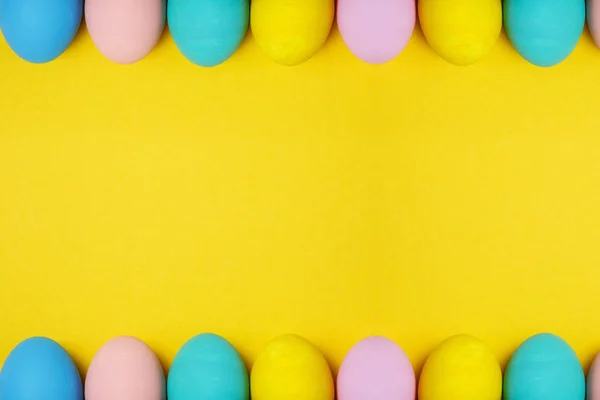 Doble fila coloridos huevos de Pascua pintados monofónicos pastel aislados sobre fondo amarillo para tarjeta o postal. Feliz concepto de Pascua. Copia espacio para la publicidad. Con lugar para el texto. Vista superior de los huevos . — Foto de Stock
