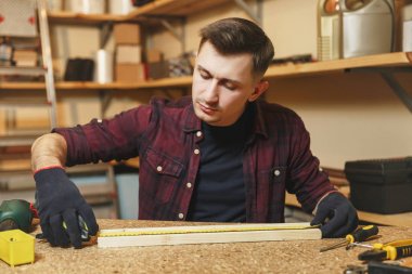 Yakışıklı beyaz delikanlı ekose gömlek, siyah T-shirt, şerit metre, ahşap masa doğrama atölyesinde çalışan ile ahşap parça uzunluğu ölçme eldiven farklı çalışma araçları ile yerleştirin..