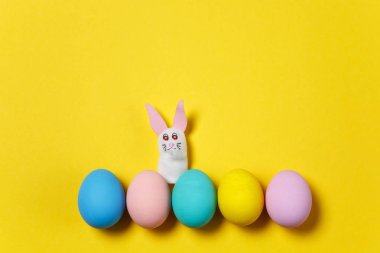 Satır beş renkli pastel tek sesli Paskalya yumurtaları sarı arka plan, beyaz tavşan veya tavşan izole boyalı. Mutlu Paskalya kavramı. Reklam için yer kopyalayın. Metin için yer ile. Yumurta üzerinde Üstten Görünüm.