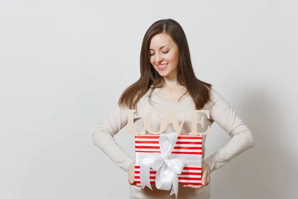 Belle jeune femme souriante sexy tenant boîte cadeau rouge avec cadeau, mot en bois amour sur fond blanc. Espace de copie pour la publicité. Saint-Valentin ou concept de Journée internationale de la femme . — Photo