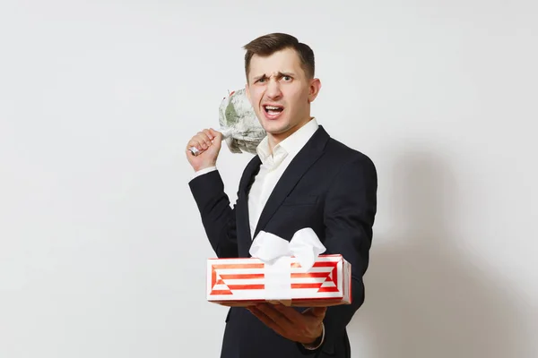 Young crazy angry perturbed man in suit holding bouquet of roses flowers, red present box with gift isolated on white background. St. Valentine's Day, International Women Day birthday holiday concept. — Stock Photo, Image