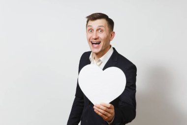 Beyaz arka plan üzerinde izole büyük beyaz kalp tutan takım elbiseli genç yakışıklı adam. Alan, reklam kopyalayın. Metin için yer. St. Valentine's Day, Dünya Kadınlar Günü, doğum günü, konsept tatil.
