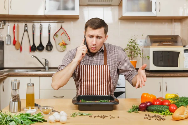 Perturbed stress young man in apron sitting at table with vegeta — Stock Photo, Image