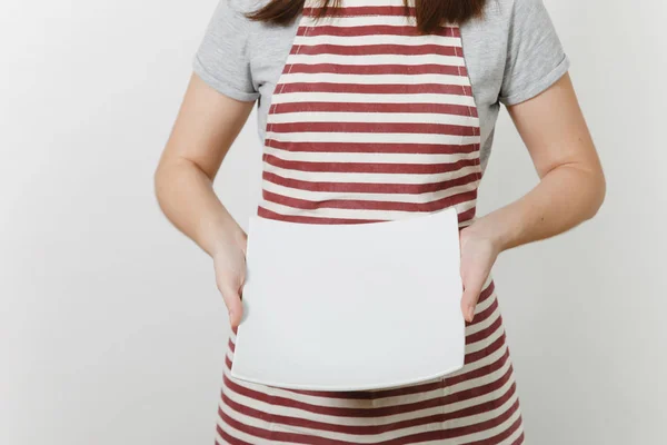 Young caucasian housewife in striped apron, gray t-shirt isolated on white background. Housekeeper woman holding in hands white empty square plate. Copy space for advertisement. — Stock Photo, Image