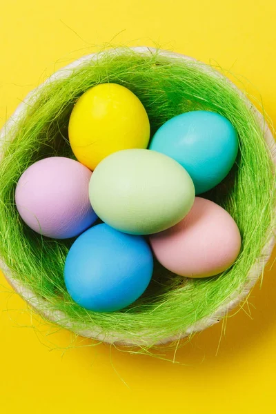 Vertical seis pastel colorido pintado ovos de Páscoa em cesta com grama verde isolado no fundo amarelo. Feliz conceito de Páscoa. Espaço de cópia para propaganda. Com lugar para SMS. Vista superior em ovos . — Fotografia de Stock