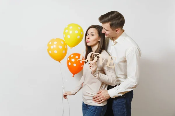 Cute couple in love. Man, woman with wooden word Love, yellow, orange balloons isolated on white background. For advertisement. St. Valentine's Day, International Women's Day, birthday holiday concept — Stock Photo, Image