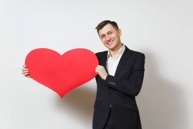Beyaz arka plan üzerinde izole büyük kırmızı kalp tutan takım elbiseli genç gülümseyen adam. Alan, reklam kopyalayın. Metin için yer. St. Valentine's Day, Dünya Kadınlar Günü, doğum günü, konsept tatil.