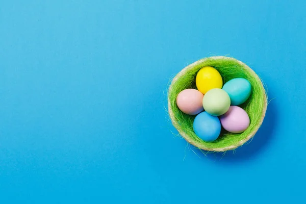 Seis coloridos pastel monofônico pintado ovos de Páscoa em cesta com grama verde isolado no fundo azul. Feliz conceito de Páscoa. Espaço de cópia para propaganda. Com lugar para SMS. Vista superior em ovos . — Fotografia de Stock