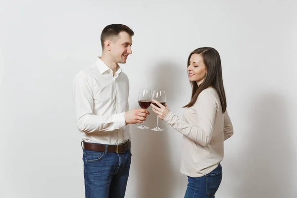 Young caucasian couple. Happy smiling man and woman in love in casual light clothes, jeans making toast, drinking from glasses of red wine isolated on white background. Copy space for advertisement. — Stock Photo, Image