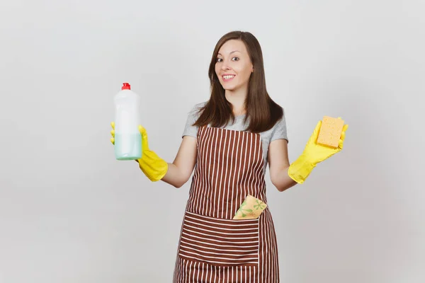 Young housewife in yellow gloves, striped apron, cleaning rag in pocket isolated on white background. Woman holding bottle with cleaner liquid for washing dishes, sponge. Copy space for advertisement.