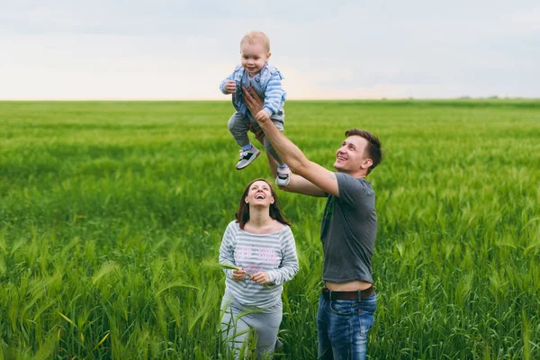 Fröhlicher Mann, Frau gehen auf der grünen Wiese Hintergrund, Ruhe, Spaß haben, spielen, werfen kleine niedliche Kind Baby Boy. Mutter, Vater, kleiner Sohn. Familientag 15. Mai, Liebe, Eltern, Kinder. — Stockfoto