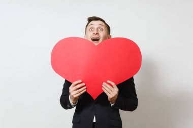 Genç beyaz arka plan üzerinde izole büyük kırmızı kalp arkasına saklanmış takım elbiseli adam eğlenceli. Alan, reklam kopyalayın. Metin için yer. St. Valentine's Day, Dünya Kadınlar Günü, doğum günü, konsept tatil.