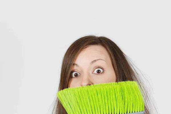 Primo piano di giovane divertimento pazzo vertigini pazzo selvaggio spaventato casalinga con i capelli arruffati isolato su sfondo bianco. Donna pazza governante che si nasconde dietro una scopa verde. Copia spazio per pubblicità . — Foto Stock