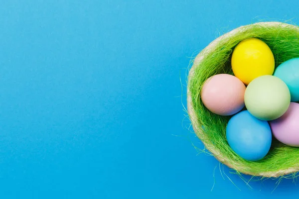 Seis coloridos pastel monofônico pintado ovos de Páscoa em cesta com grama verde isolado no fundo azul. Feliz conceito de Páscoa. Espaço de cópia para propaganda. Com lugar para SMS. Vista superior em ovos . — Fotografia de Stock