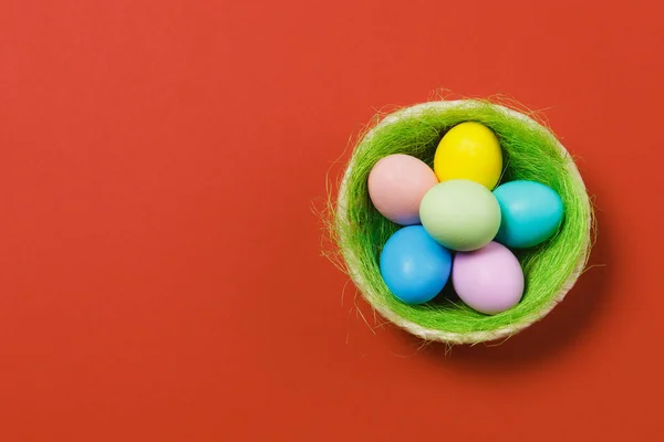 Zes kleurrijke pastel monofone geverfde paaseieren in de mand met groen gras geïsoleerd op rode achtergrond. Gelukkig Pasen concept. Kopiëren van ruimte voor reclame. Met de plek voor tekst. Bovenaanzicht op eieren. — Stockfoto