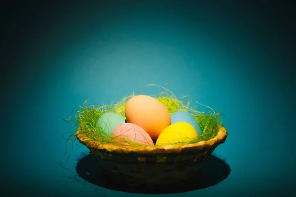 Colorido pastel monofônico tradicional pintado ovos de Páscoa em cesta com grama verde no fundo azul escuro com sombras pretas, silhueta, luz. Espaço de cópia para propaganda. Com lugar para texto — Fotografia de Stock