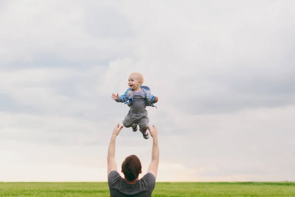 Fröhliche Mann zu Fuß auf der grünen Wiese, Ruhe, Spaß haben, spielen, werfen hoch kleine süße Kind Baby Junge auf Himmel Hintergrund. Vater wirft kleinen Sohn hin. Familientag 15. Mai, Liebe, Eltern, Kinder. — Stockfoto