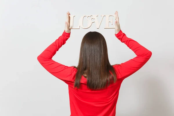 Young woman in red casual clothes turning back to camera, holding wooden word love above head on white background. Copy space for advertisement. St. Valentines Day or International Women s Day concept