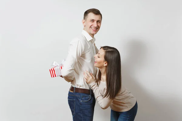 Cute fun couple in love. Woman looking behind man who hiding behind him red present box with gift isolated on white background. St. Valentine's Day, International Women's Day birthday holiday concept — Stock Photo, Image