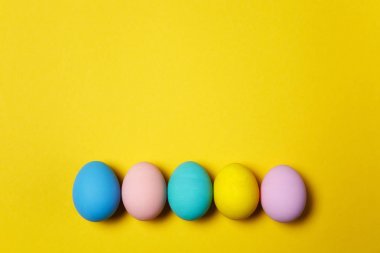 Satır kartı veya kartpostal Sarı zemin üzerine izole beş renkli pastel tek sesli boyalı Paskalya yumurta. Mutlu Paskalya kavramı. Reklam için yer kopyalayın. Metin için yer ile. Yumurta üzerinde Üstten Görünüm