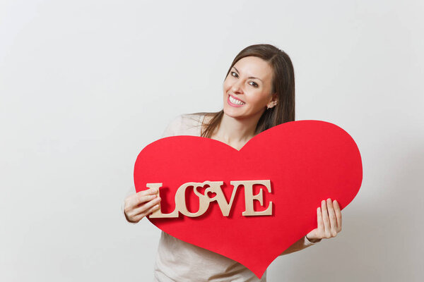 Effective young smiling woman holding big red heart, wooden word love on white background. Copy space for advertisement. With place for text. St. Valentine's Day or International Women's Day concept.
