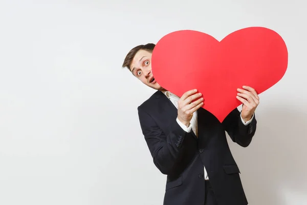 Young fun man in suit hiding behind big red heart isolated on white background. Copy space, advertisement. Place for text. St. Valentine's Day, International Women's Day, birthday, holiday concept. — Stock Photo, Image