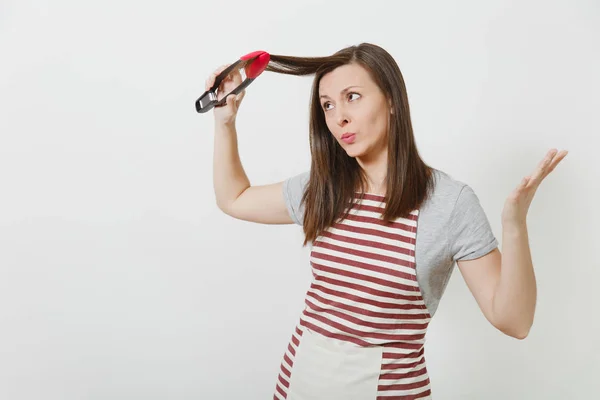 Young fun attractive smiling brunette caucasian housewife in striped apron isolated on white background. Beautiful housekeeper woman holding hair by kitchen tongs like styler curling hair. — Stock Photo, Image