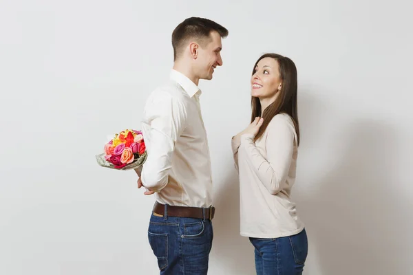 Couple in love. Woman looking behind man who hiding behind him bouquet of beautiful roses flowers isolated on white background. St. Valentine's Day, International Women's Day birthday holiday concept — Stock Photo, Image