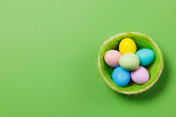 Zes kleurrijke pastel monofone geverfde paaseieren in de mand met groen gras geïsoleerd op groene achtergrond. Gelukkig Pasen concept. Kopiëren van ruimte voor reclame. Met de plek voor tekst. Bovenaanzicht op eieren. — Stockfoto