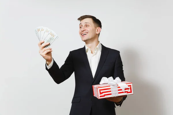 Jeune bel homme en costume tenant boîte cadeau rouge avec cadeau, paquet de dollars d'argent en espèces isolé sur fond blanc. Saint-Valentin, Journée internationale de la femme, concept de fête d'anniversaire . — Photo