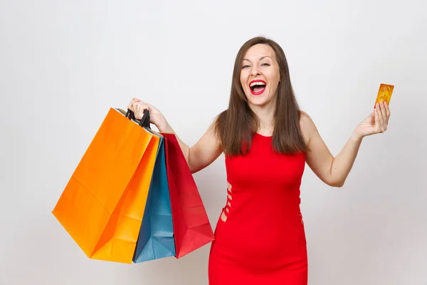 Αρκετά εντυπωσιακό μοντέρνο νεαρή γυναίκα καφέ-μαλλιά σε κόκκινο φόρεμα εκμετάλλευση πιστωτική κάρτα, multi έγχρωμο πακέτα με αγορές μετά ψώνια απομονώνονται σε λευκό φόντο. Αντίγραφο χώρος για διαφήμιση. — Φωτογραφία Αρχείου
